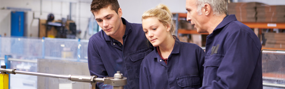 Two apprentices in work clothes listening to an instructor's advice